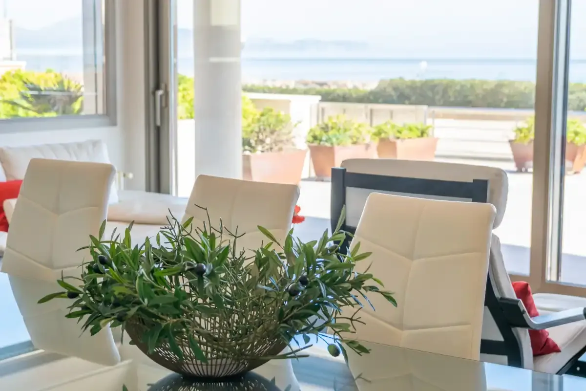 A dining area with white seating and a glass table faces a bright terrace.