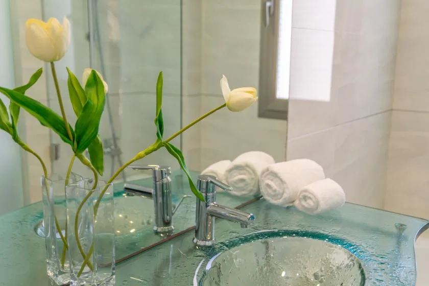 A bathroom vanity with a glass sink, mirrored wall, and rolled towels.