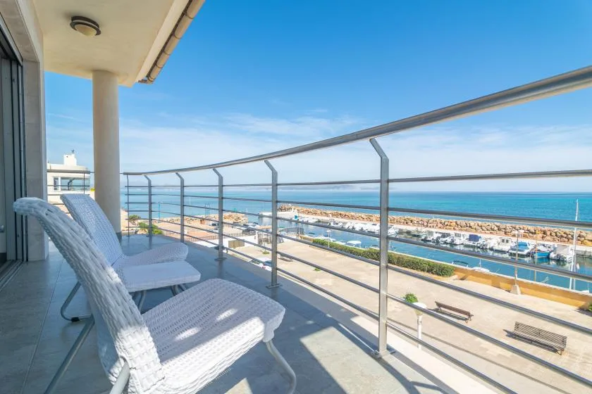 A balcony overlooks the sea, with white lounge seating beside the railing.