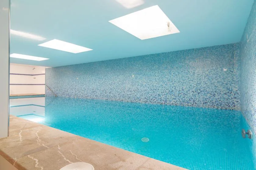 An indoor swimming pool with blue-tiled walls and bright ceiling lights.