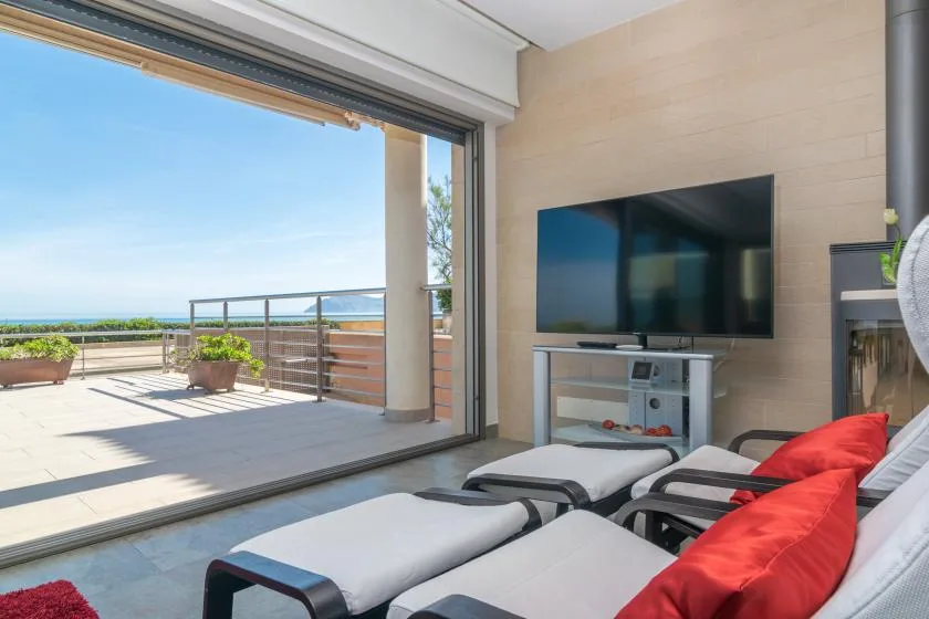 A lounge opens onto a bright terrace with seating and a sea view.