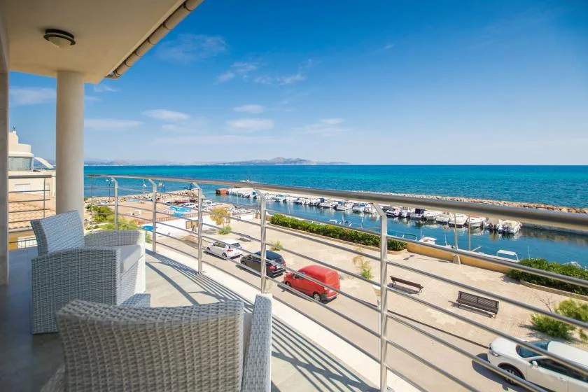 A balcony overlooks a marina and the sea, with outdoor seating beside the railing.