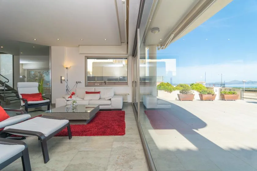 A modern living room opens onto a sunny terrace through broad glass doors.