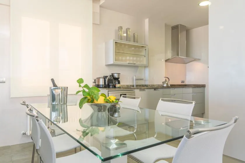 A modern kitchen with a glass dining table and white seating.