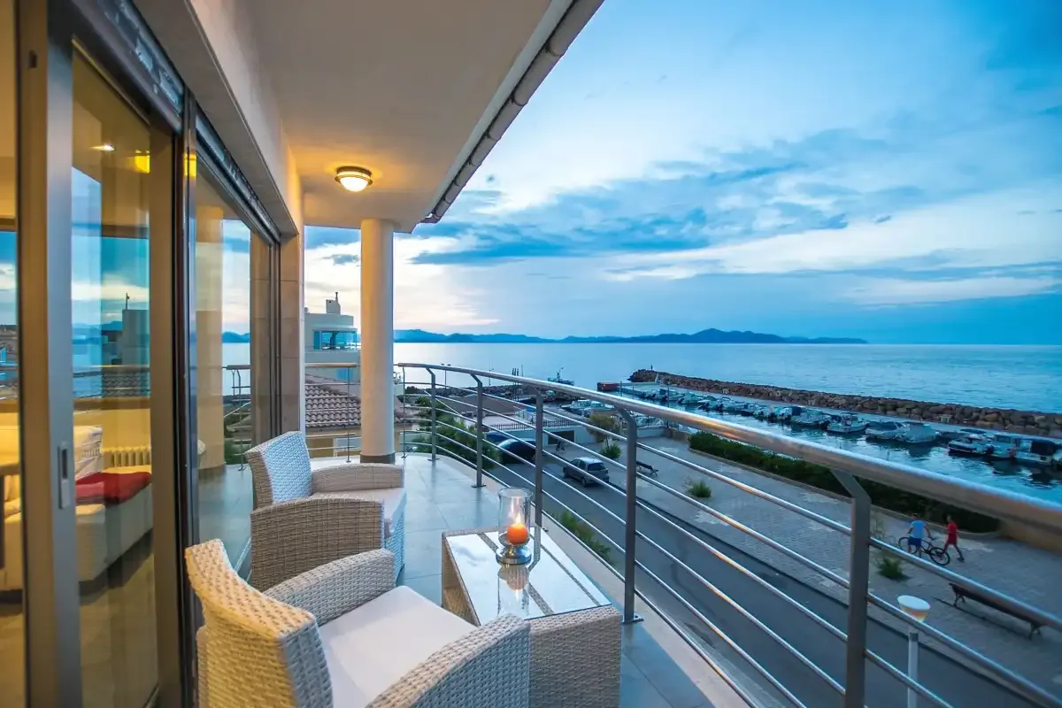A furnished balcony overlooks a coastal promenade and the sea.