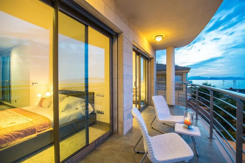 A balcony seating area overlooks the sea beside floor-to-ceiling glass doors.