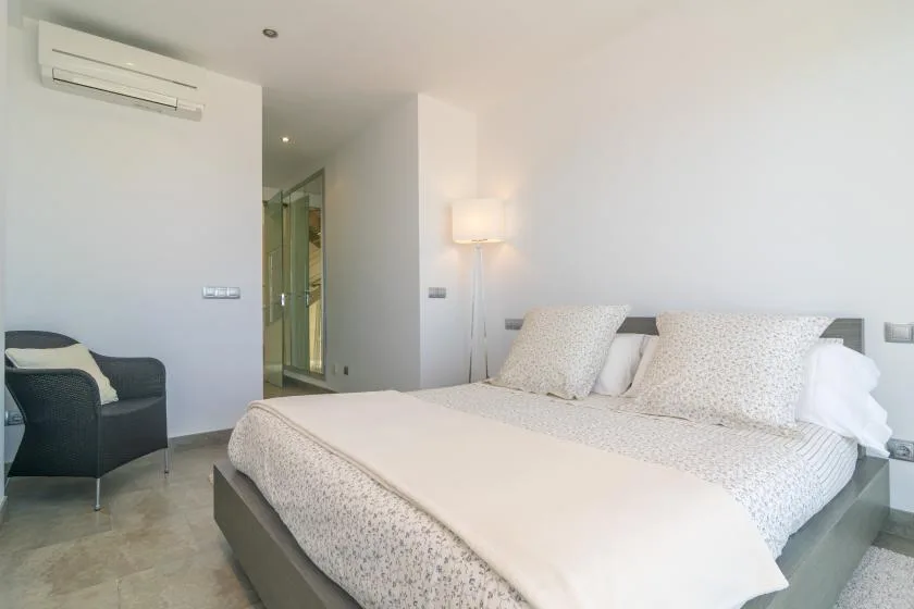 A bright bedroom with a large bed and a dark armchair.