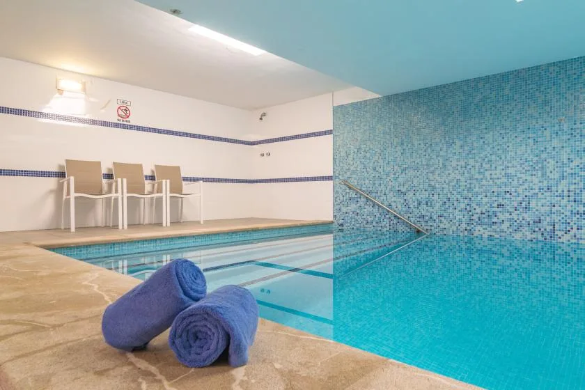 An indoor swimming pool with blue mosaic-tile walls and rolled towels on the deck.