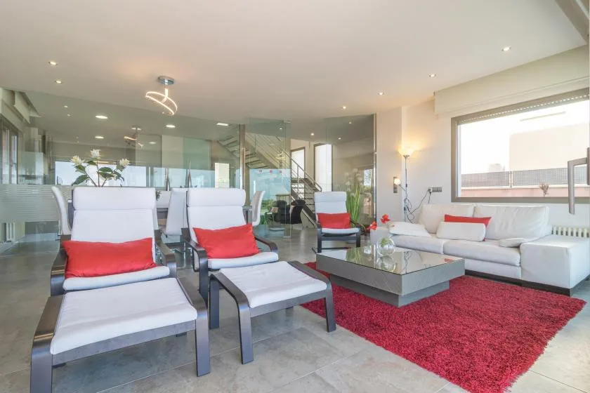 A modern lounge with white seating, a glass coffee table, and a red rug.