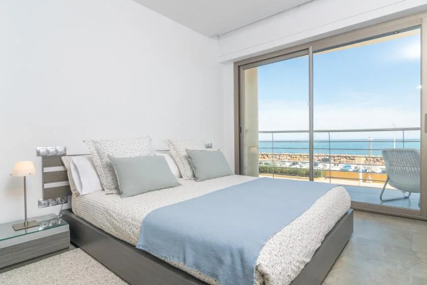 A bedroom with a neatly made bed beside large windows overlooking the sea.