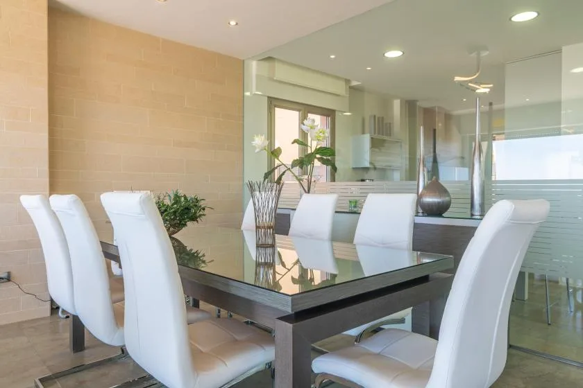 A modern dining area with a glass table and white seating.
