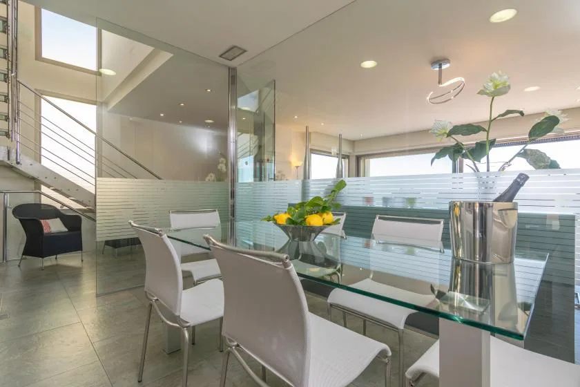 A bright dining area with a glass table and white seating beside large windows.