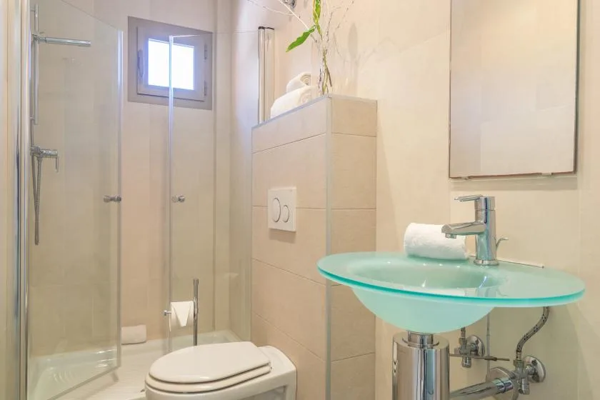 A bathroom with a glass shower, toilet, and turquoise glass sink.