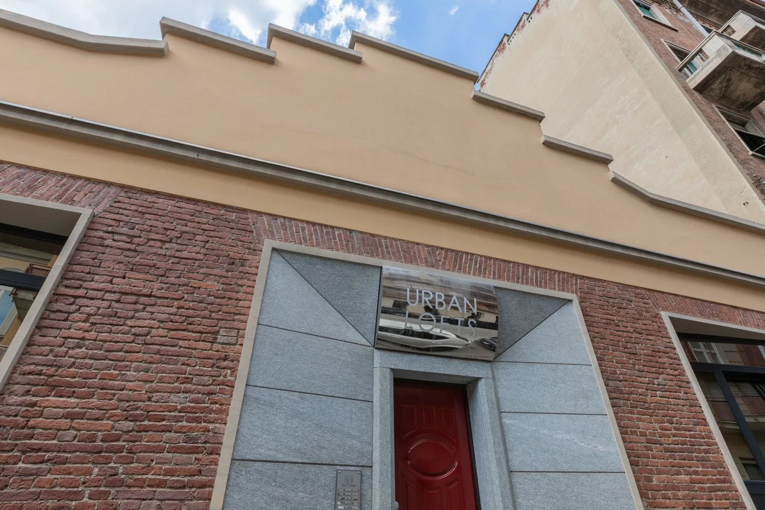 A brick building facade with a red entrance door and a sign above it.