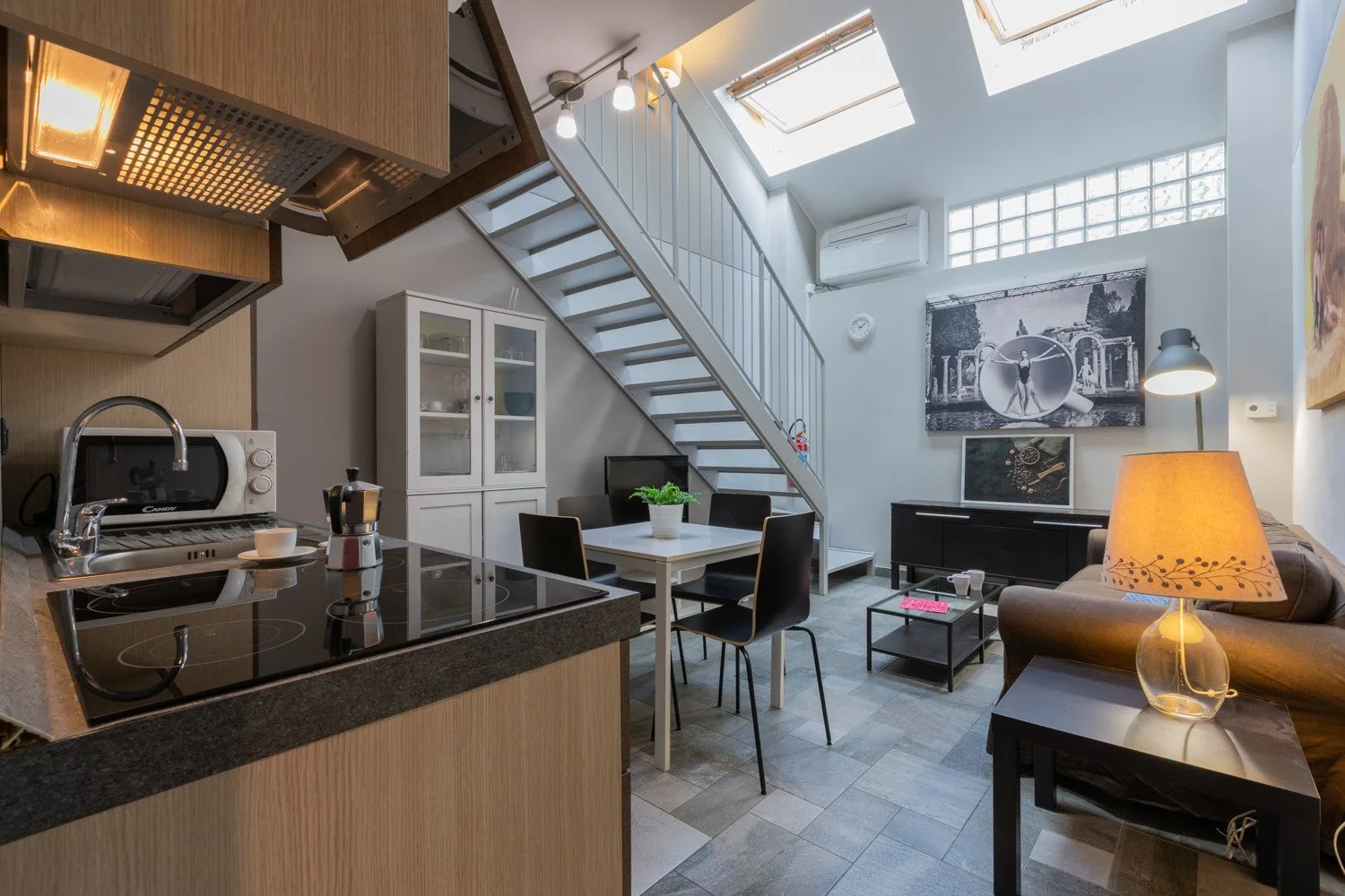 An open-plan living area with a kitchen counter, dining table, and seating beneath a staircase.