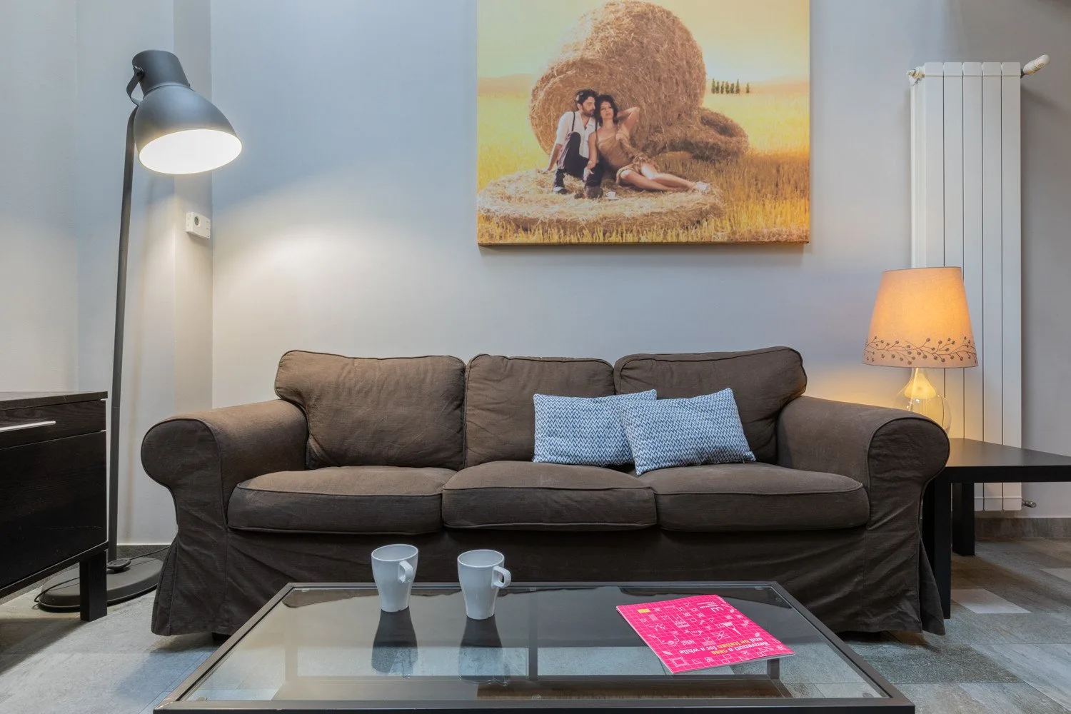 A living room with a dark sofa, glass coffee table, and wall art.