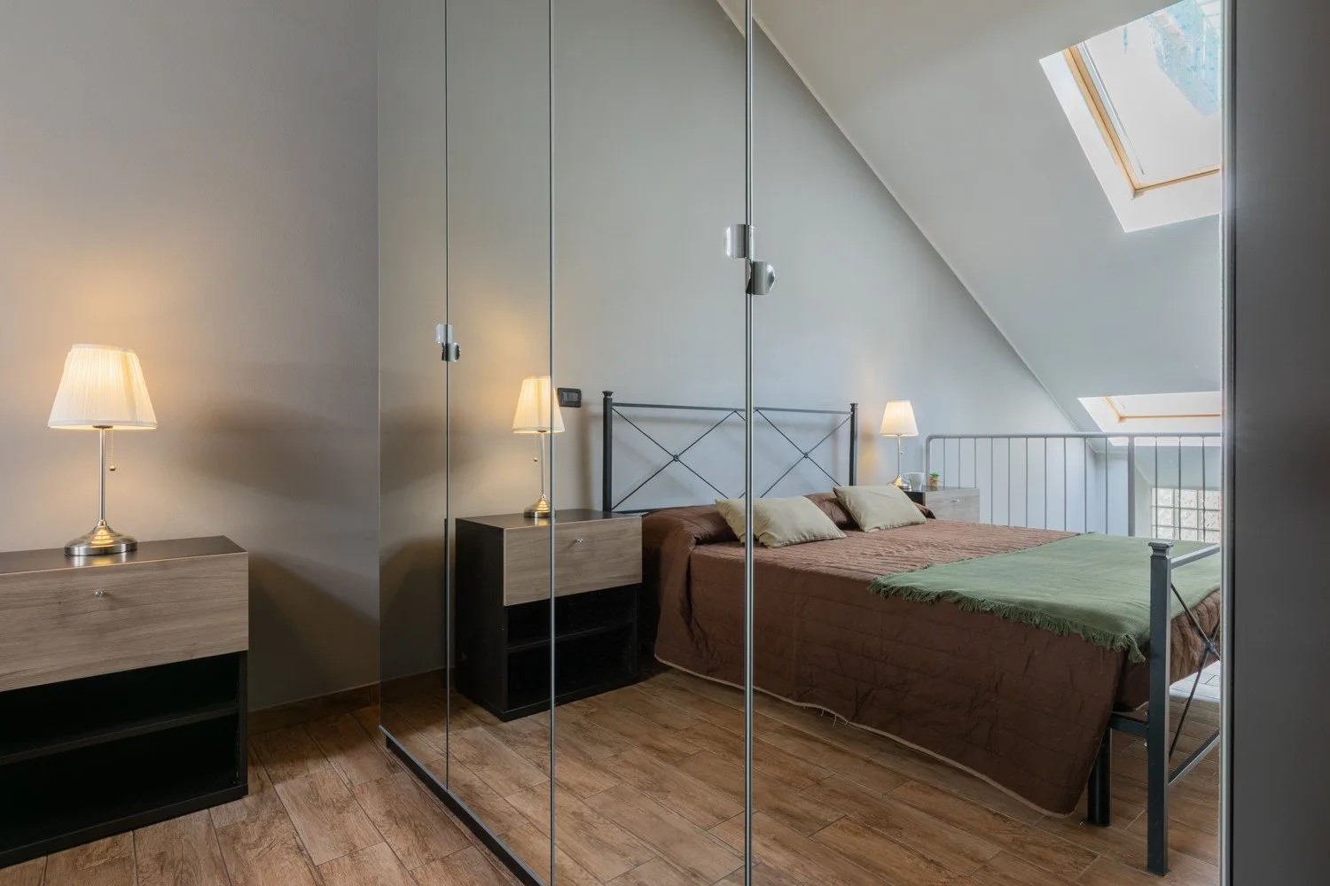 A bedroom with a double bed, mirrored wardrobe, and bedside lamps.