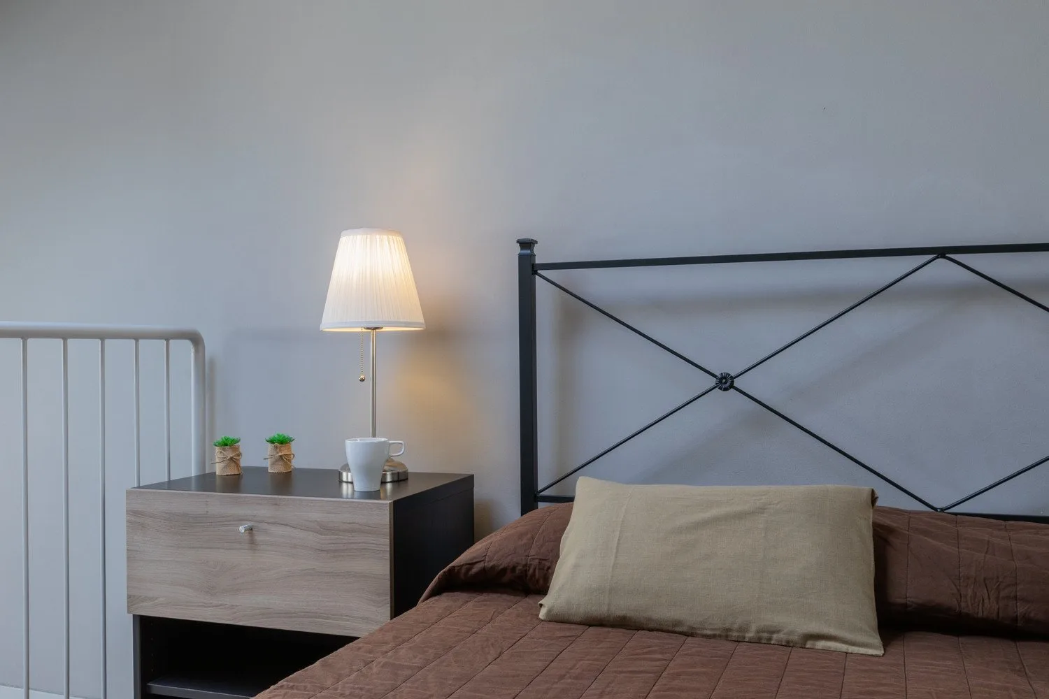 A bedroom with a bed, dark metal headboard, and bedside table with a lamp.