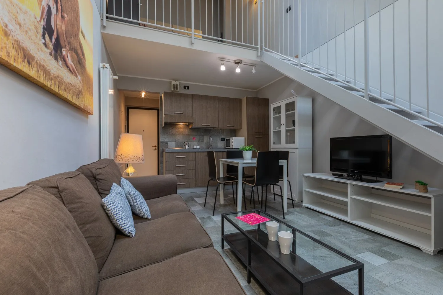 A living area with seating, a television, and a dining table beneath a staircase.