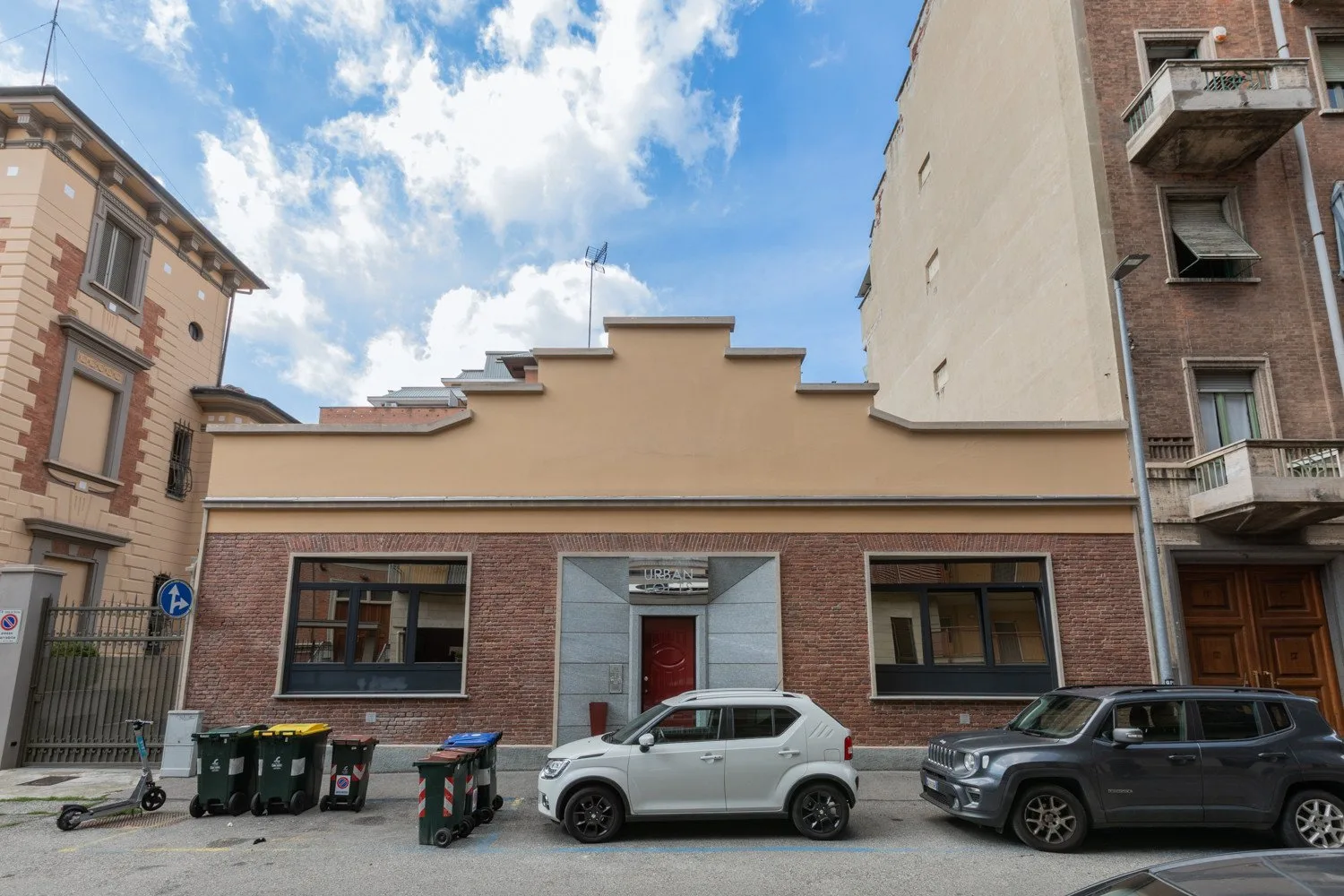 A street-facing building with a stepped roofline and parked cars in front.