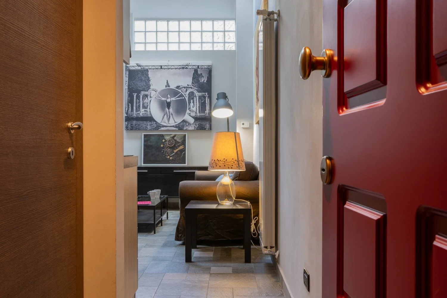 A view through an open doorway into a living room with seating and a lit table lamp.
