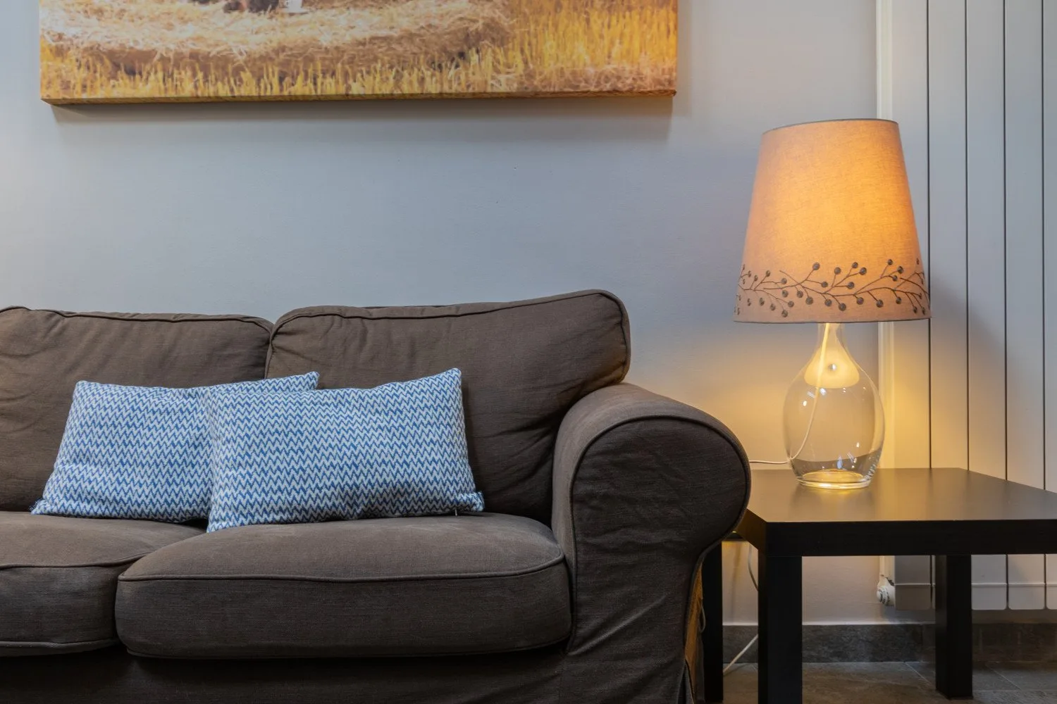 A living room seating area with patterned cushions and a lit table lamp.
