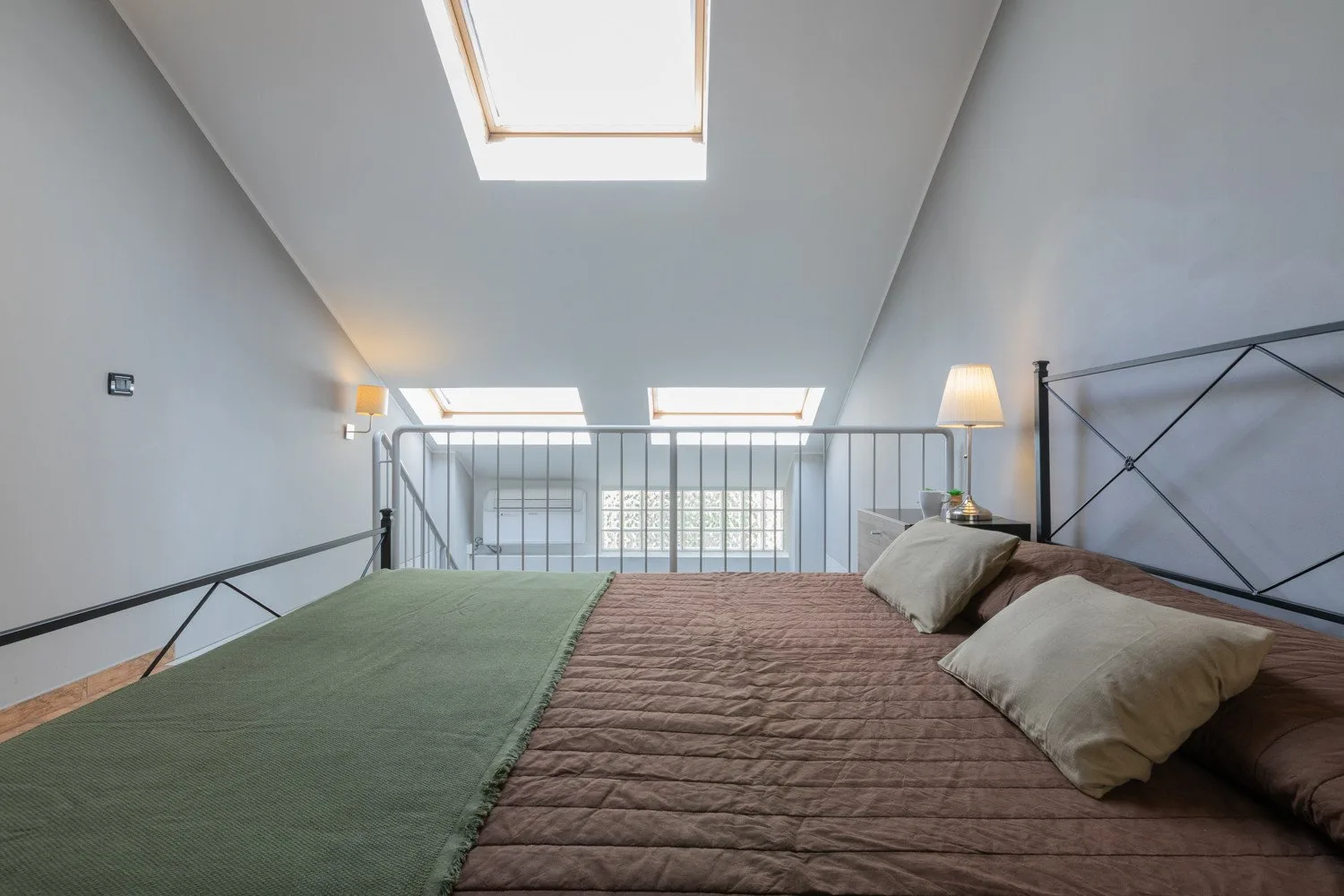 A loft bedroom with a bed beneath skylights and a metal railing.