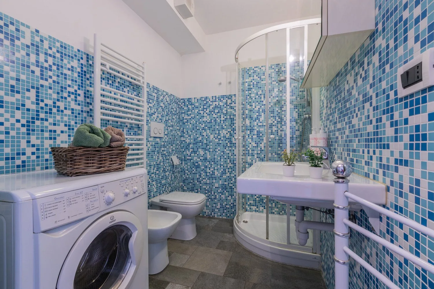 A tiled bathroom with a curved glass shower, sink, toilet, and washing machine.