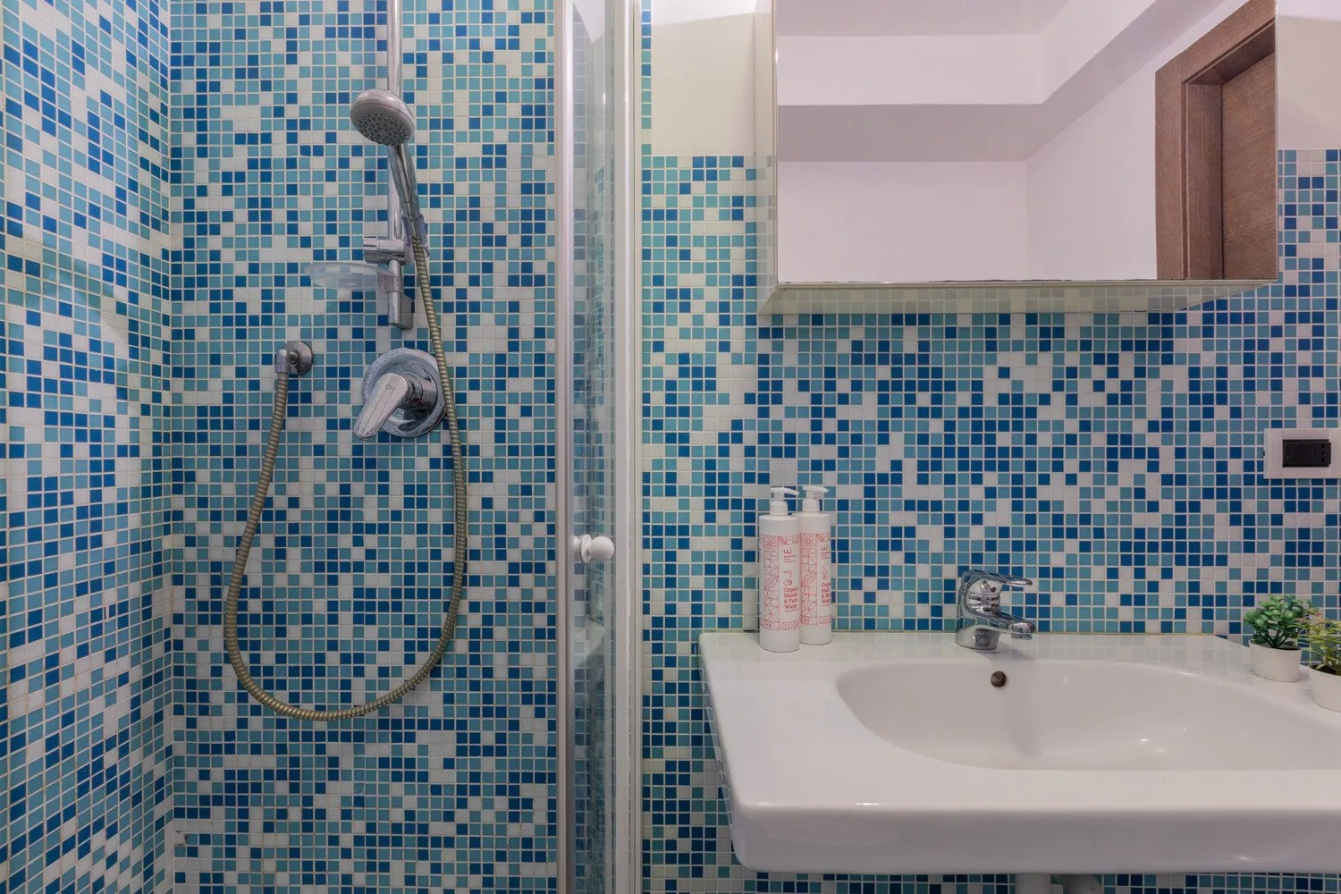 A tiled bathroom with a shower and sink beneath a mirror.