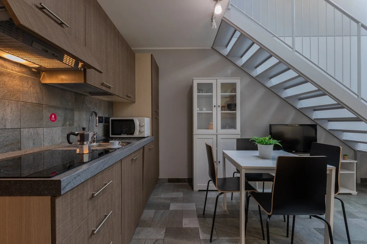 A modern kitchen and dining area sits beneath an open staircase.