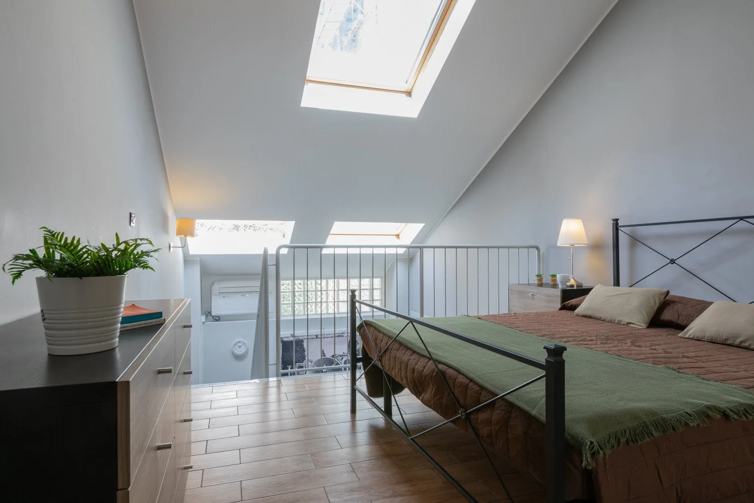 A bright attic bedroom has a double bed beneath sloped ceilings and skylights.