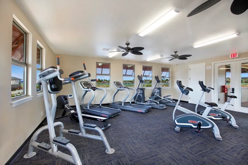 Una sala de ejercicio con cintas de correr y bicicletas junto a las ventanas.