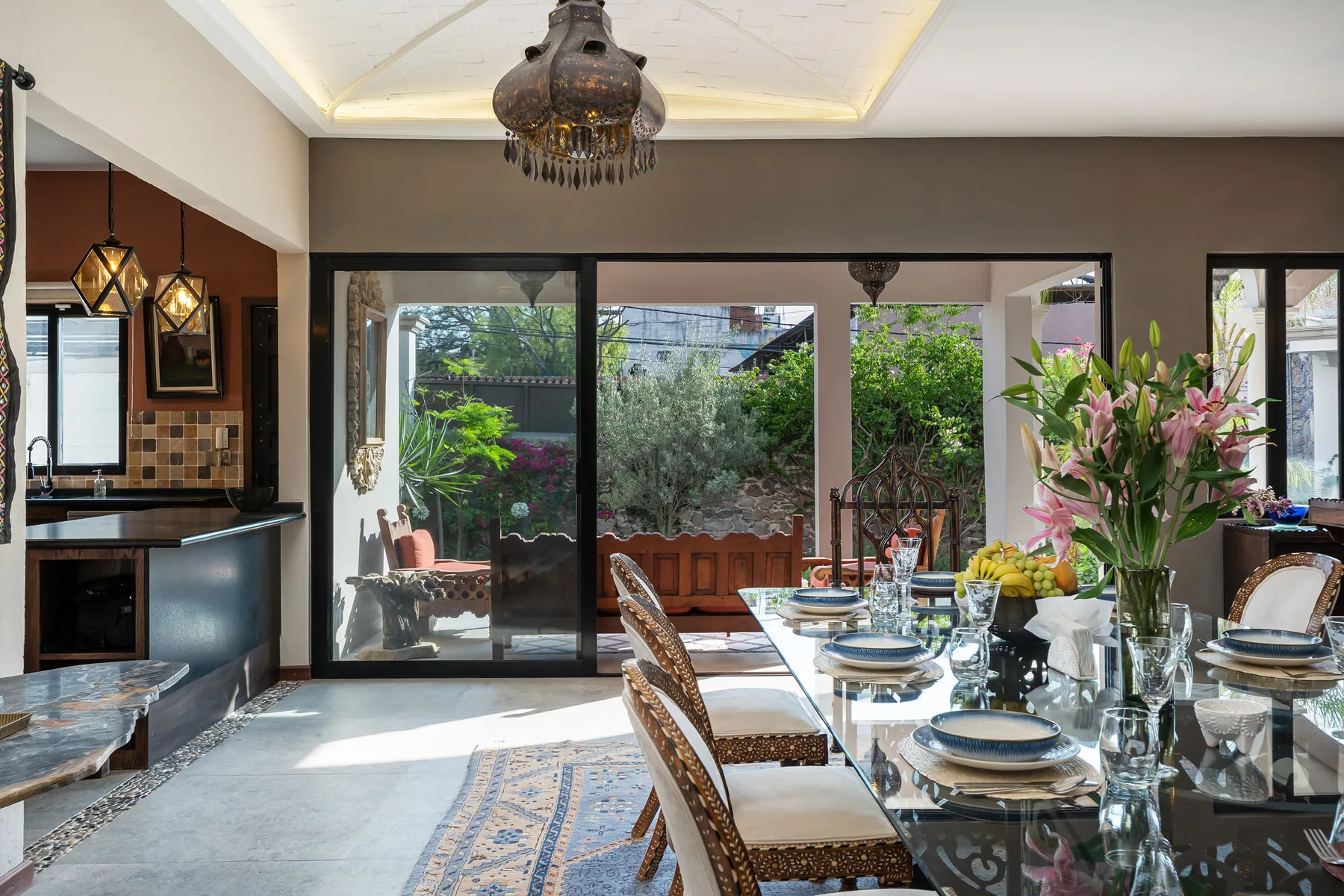 A dining area with a set table beside large glass doors opening onto a leafy garden.
