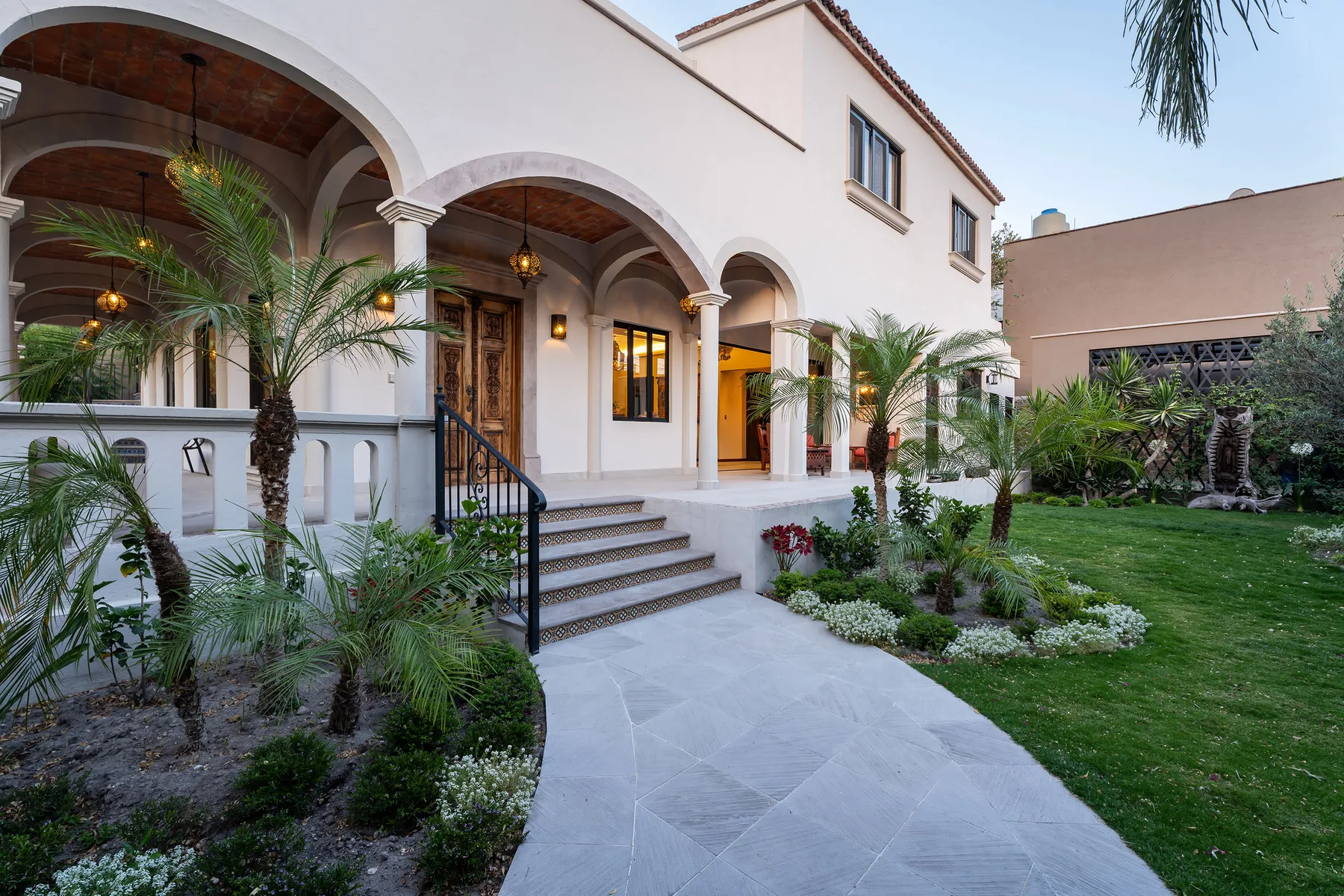A stucco house entrance with arched porches and a landscaped garden.