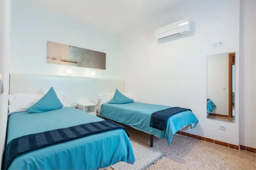 A bright bedroom with two beds dressed in turquoise bedding.