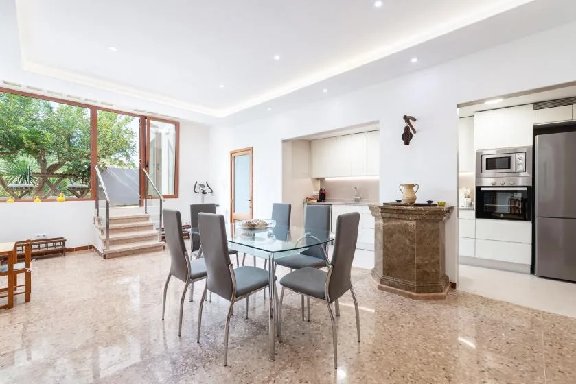 A bright dining area with a glass table beside the kitchen and large windows.