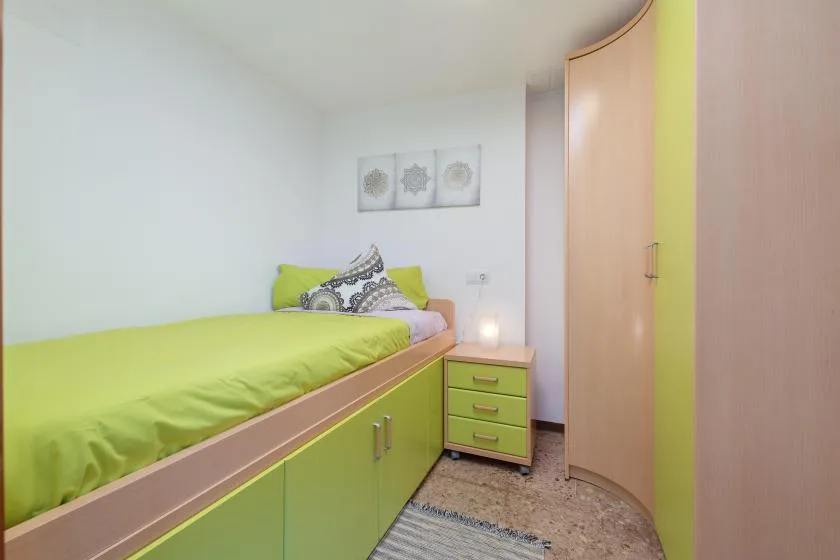 A bedroom with a lime-green bed, matching storage drawers, and a tall wardrobe.