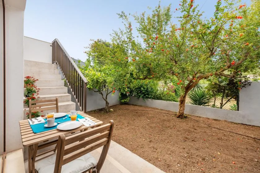 A small outdoor patio with a wooden dining table beside a garden tree.