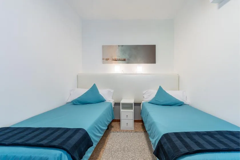 A bright bedroom with two beds and a small nightstand between them.