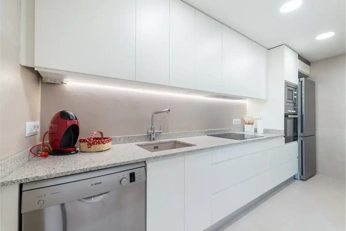 A bright modern kitchen with white cabinets and a long countertop.