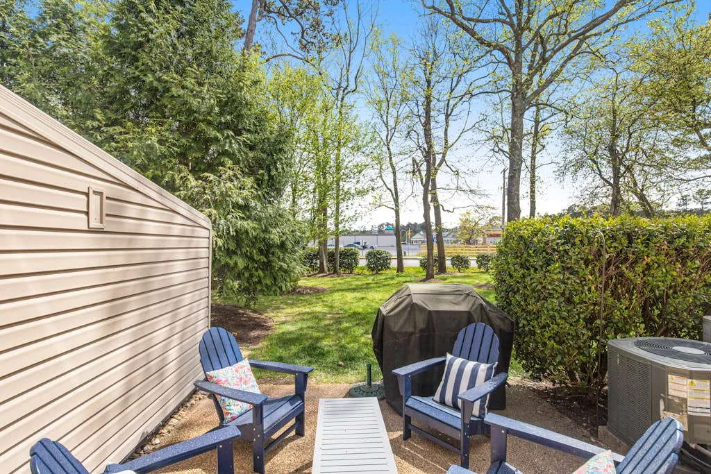 An outdoor seating area beside a shed, with trees and a hedge beyond.