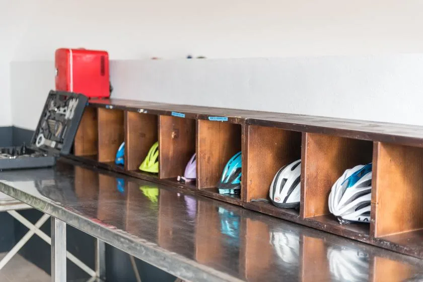 A row of wooden storage cubbies holds helmets above a long counter.