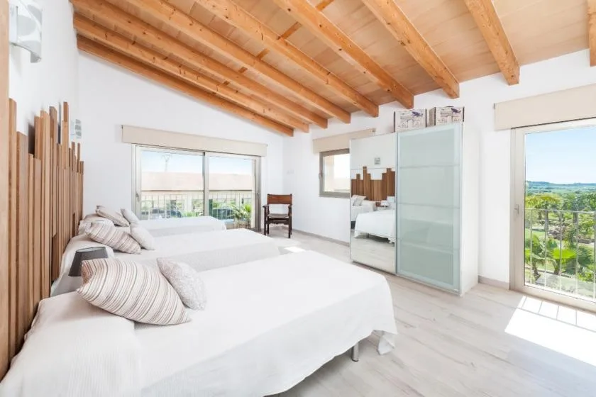 A bright bedroom with white bedding, a mirrored wardrobe, and large windows.