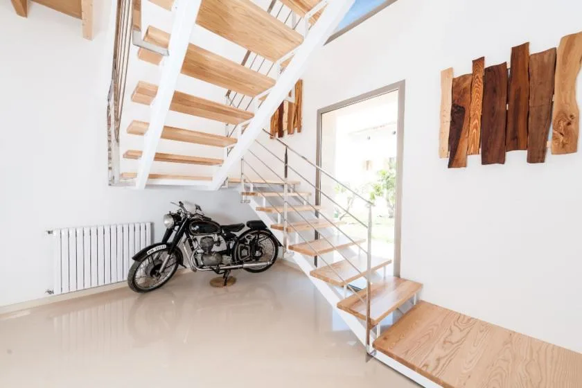 A bright interior with an open wooden staircase and a motorcycle beneath it.