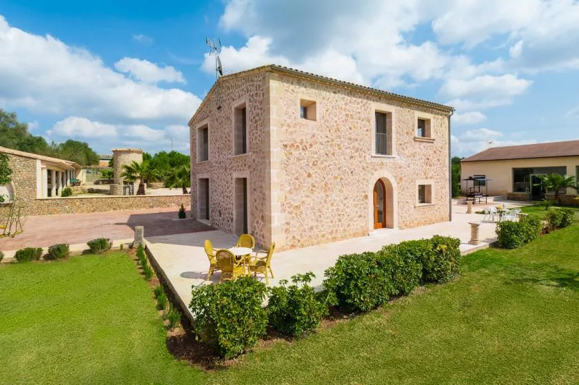 A two-story stone house stands beside a lawn, with outdoor seating on the patio.
