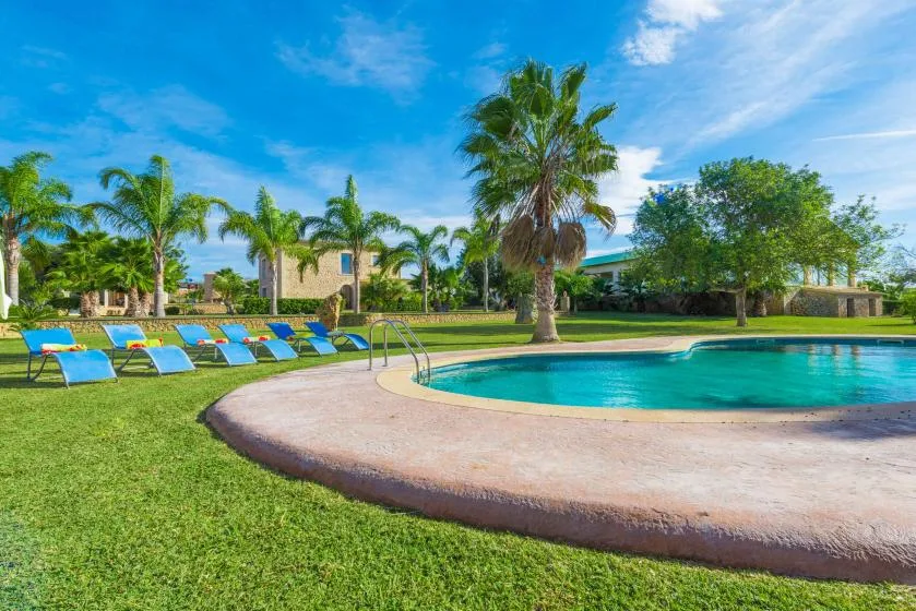 An outdoor swimming pool curves beside a grassy lawn and several lounge chairs.