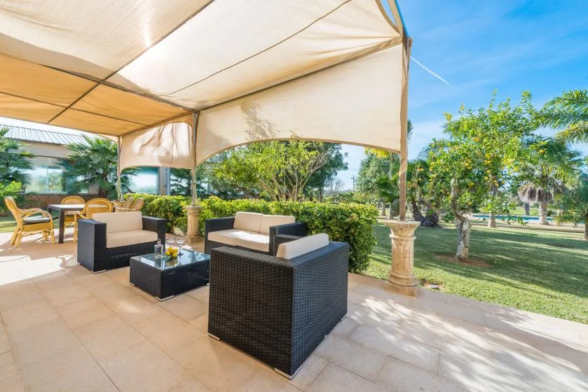 A covered outdoor patio with cushioned seating overlooks a garden.