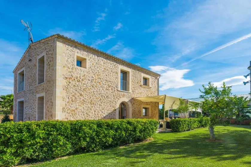 A stone house stands beside a green lawn under a blue sky.