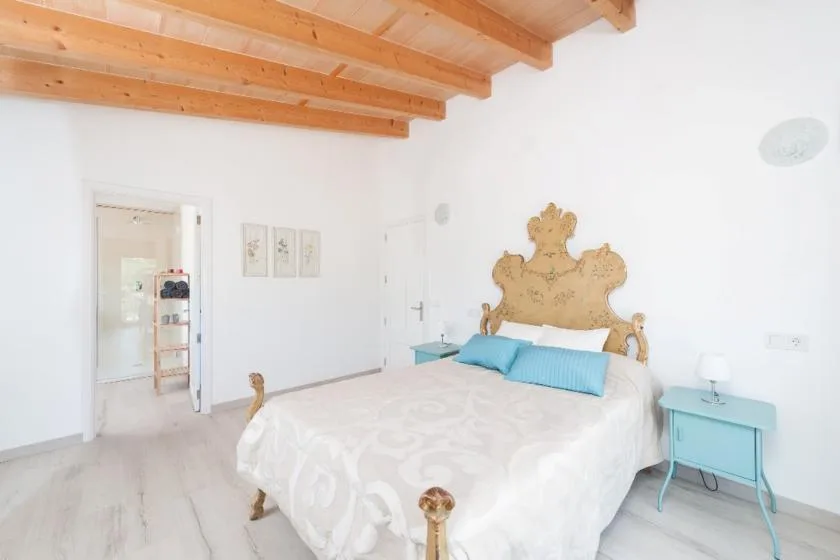 A bedroom with a bed beneath exposed wooden ceiling beams and a turquoise bedside table.