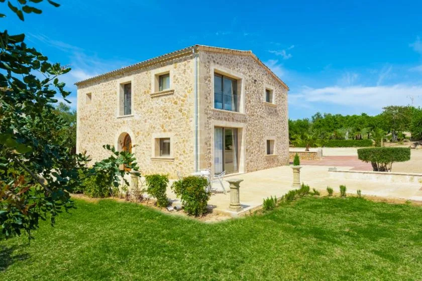 A stone house stands beside a paved patio and green lawn.
